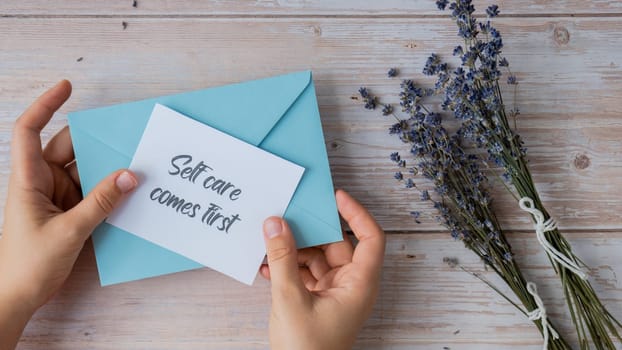 SELF CARE COMES FIRST text on supportive message paper note reminder from blue envelope. Flat lay composition dry lavender flowers. Concept of inner happiness, slowing-down digital detox personal fulfillment. Top view
