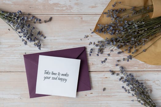 Paper card note with text TAKE TIME TO MAKE YOUR SOUL HAPPY from violet envelope. Lavender flower. Top view, flat lay. Concept of mental spiritual health self care wellbeing mindfulness