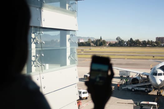 Woman holding mobile phone and taking picture of the plane at an international airport