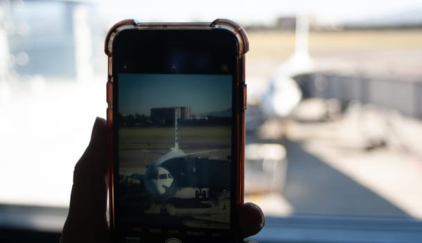 Hand holding mobile phone and taking picture of the plane at the airport