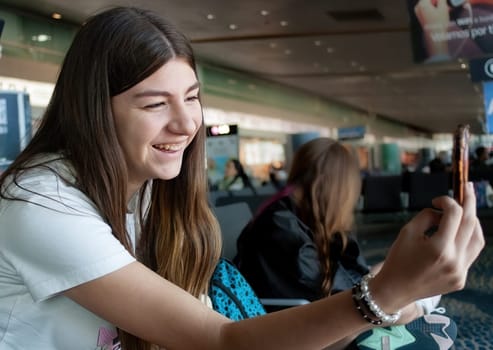 A teenager is chatting on her mobile phone in an international airport terminal.