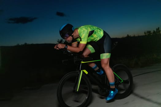 A triathlete rides his bike in the darkness of night, pushing himself to prepare for a marathon. The contrast between the darkness and the light of his bike creates a sense of drama and highlights the athlete's determination and perseverance