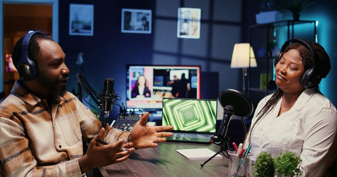 African american host engaging in entertaining discussion with celebrity during live stream in professional studio, making her laugh. Presenter uses high quality equipment to produce comedy podcast