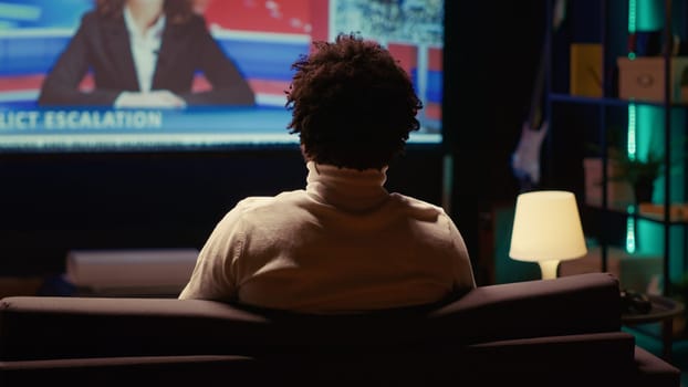 African american man watching Video on demand channel on widescreen television set in neon lit living room. Cord cutter entertained by streaming service program broadcasted on smart TV in home theatre