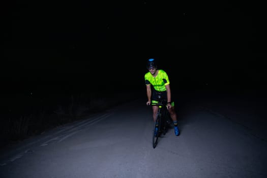 A triathlete rides his bike in the darkness of night, pushing himself to prepare for a marathon. The contrast between the darkness and the light of his bike creates a sense of drama and highlights the athlete's determination and perseverance