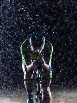 A triathlete braving the rain as he cycles through the night, preparing himself for the upcoming marathon. The blurred raindrops in the foreground and the dark, moody atmosphere in the background add to the sense of determination and grit shown by the athlete