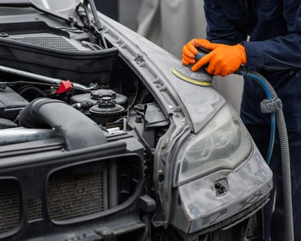 A mechanic sands the putty on a car body with a machine. Repair after an accident