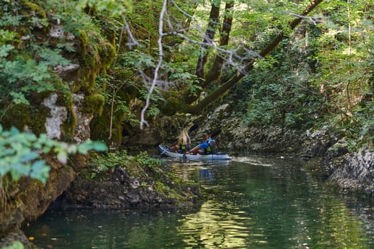 A young couple enjoying an idyllic kayak ride in the middle of a beautiful river surrounded by forest greenery.