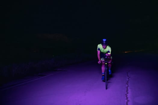 A triathlete rides his bike in the darkness of night, pushing himself to prepare for a marathon. The contrast between the darkness and the light of his bike creates a sense of drama and highlights the athlete's determination and perseverance