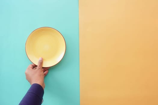 Hand Holding Yellow Plate on Split Color Background,