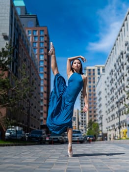 Beautiful Asian ballerina in blue dress posing in splits outdoors. Urban landscape. Vertical photo