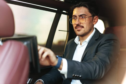Young elegant businessman watching TV on the screen in luxury car close up