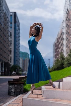 Beautiful Asian ballerina in blue dress posing on stairs outdoors. Urban landscape. Vertical photo