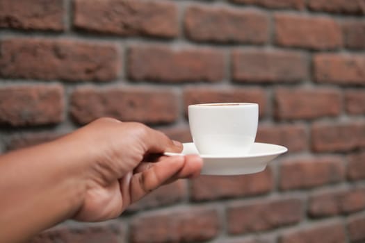 man holding a coffee cup against brick wall .