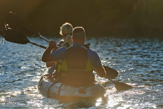 A young couple enjoying an idyllic kayak ride in the middle of a beautiful river surrounded by forest greenery in sunset time.