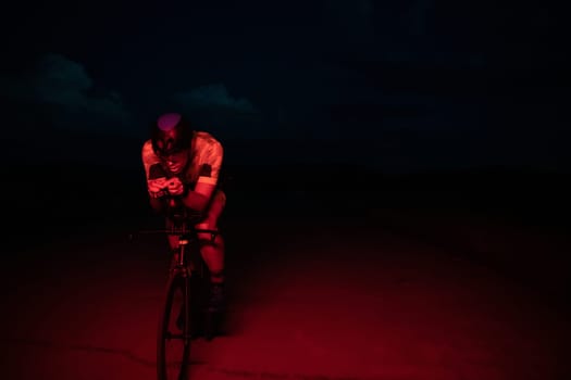 A triathlete rides his bike in the darkness of night, pushing himself to prepare for a marathon. The contrast between the darkness and the light of his bike creates a sense of drama and highlights the athlete's determination and perseverance