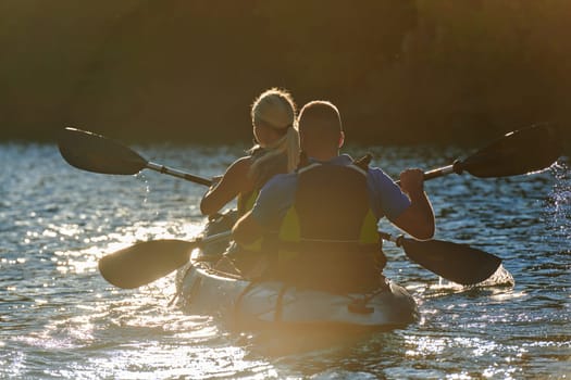 A young couple enjoying an idyllic kayak ride in the middle of a beautiful river surrounded by forest greenery in sunset time.