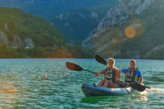 A young couple enjoying an idyllic kayak ride in the middle of a beautiful river surrounded by forest greenery in sunset time.