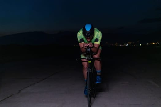 A triathlete rides his bike in the darkness of night, pushing himself to prepare for a marathon. The contrast between the darkness and the light of his bike creates a sense of drama and highlights the athlete's determination and perseverance