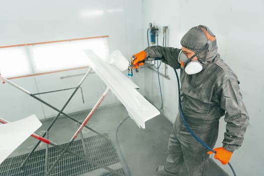 Auto painter painting a car with vaporizer gun inside a paint booth close up