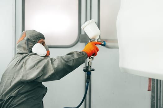 Auto painter painting a car with vaporizer gun inside a paint booth close up