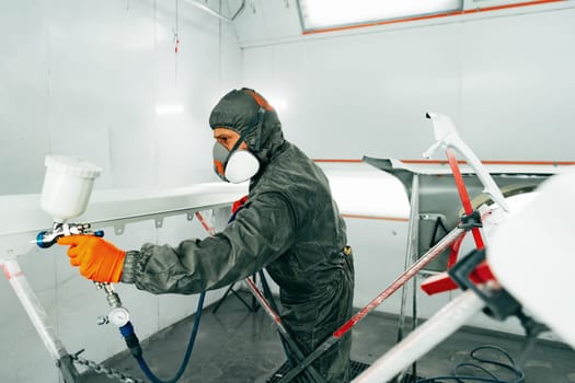 Auto painter painting a car with vaporizer gun inside a paint booth close up