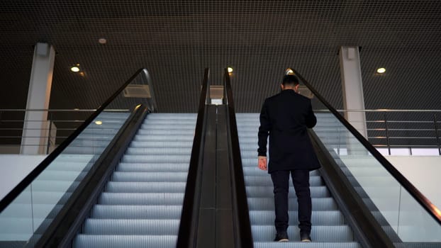 Passenger riding on the escalator up to the station of the ground metro. Media. Rear view of a young businessman on the escalator