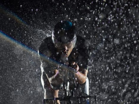 A triathlete braving the rain as he cycles through the night, preparing himself for the upcoming marathon. The blurred raindrops in the foreground and the dark, moody atmosphere in the background add to the sense of determination and grit shown by the athlete