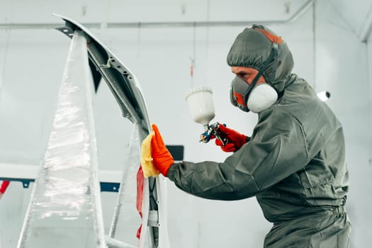 Auto mechanic worker wearing protective workwear spraying white paint on car part at workshop close up