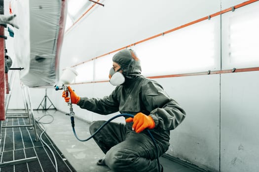 Auto painter painting a car with vaporizer gun inside a paint booth close up