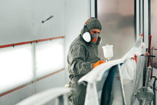 Auto painter painting a car with vaporizer gun inside a paint booth close up