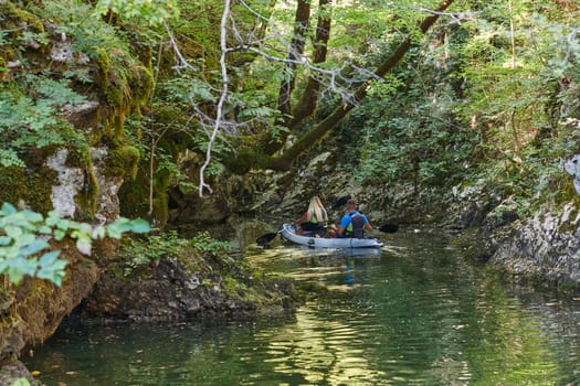 A young couple enjoying an idyllic kayak ride in the middle of a beautiful river surrounded by forest greenery.