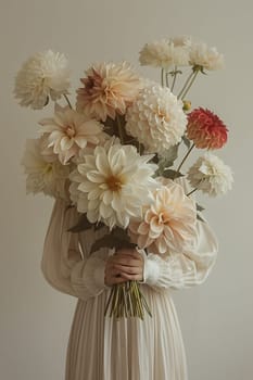 A woman in a white dress is elegantly holding a pink bouquet of flowers in front of her face, showcasing the art of flower arranging and creativity