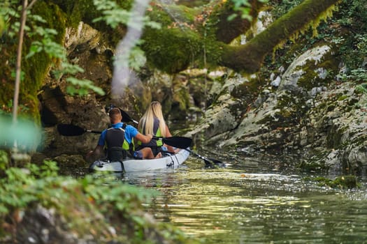 A young couple enjoying an idyllic kayak ride in the middle of a beautiful river surrounded by forest greenery.