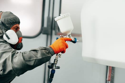 Auto painter painting a car with vaporizer gun inside a paint booth close up