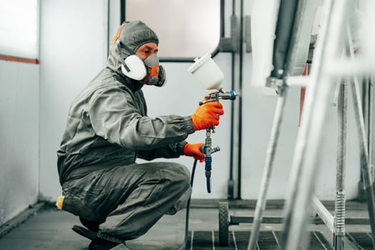 Auto painter painting a car with vaporizer gun inside a paint booth close up