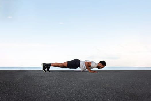 Side view of young African American male wearing sportswear doing push ups outdoors. Copy space. Active and healthy lifestyle concept.