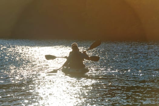 A young couple enjoying an idyllic kayak ride in the middle of a beautiful river surrounded by forest greenery in sunset time.