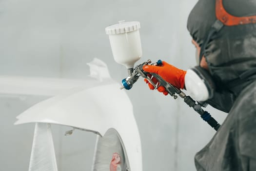 Auto painter painting a car with vaporizer gun inside a paint booth close up