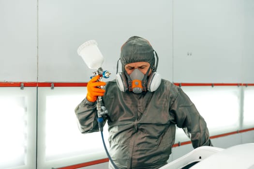 Auto mechanic worker wearing protective workwear spraying white paint on car part at workshop close up