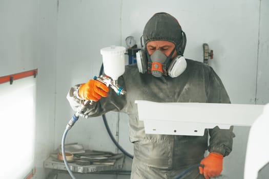 Auto painter painting a car with vaporizer gun inside a paint booth close up