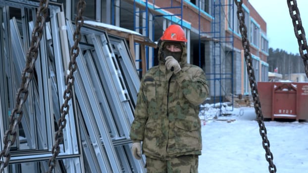 Man in helmet commands into walkie-talkie at construction site. Clip. Man talks on walkie-talkie at construction site. Contractor at construction site with walkie-talkie.