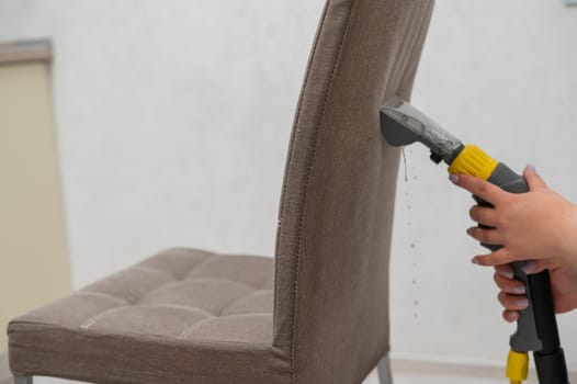 Woman cleaning the back of a fabric chair with a professional washing vacuum cleaner