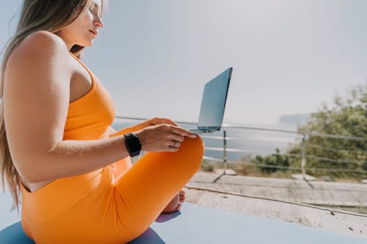 Digital nomad, Business woman working on laptop by the sea. Pretty lady typing on computer by the sea at sunset, makes a business transaction online from a distance. Freelance, remote work on vacation