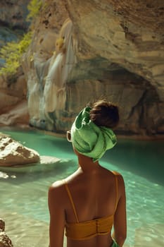 A woman wearing swimwear stands in front of a picturesque waterfall, surrounded by the beauty of nature and fluvial landforms of streams