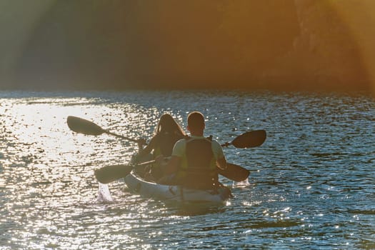 A young couple enjoying an idyllic kayak ride in the middle of a beautiful river surrounded by forest greenery in sunset time.