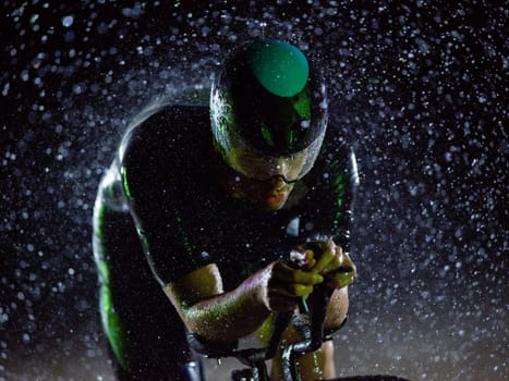 A triathlete braving the rain as he cycles through the night, preparing himself for the upcoming marathon. The blurred raindrops in the foreground and the dark, moody atmosphere in the background add to the sense of determination and grit shown by the athlete