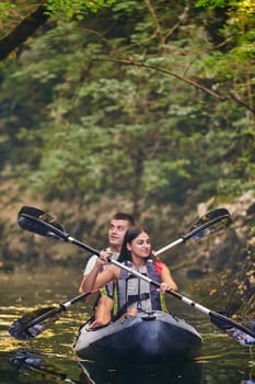 A young couple enjoying an idyllic kayak ride in the middle of a beautiful river surrounded by forest greenery.