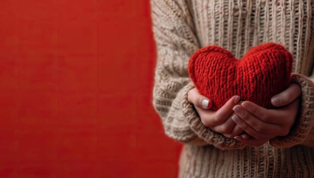 Female hands holding a red heart on a red background with copy space