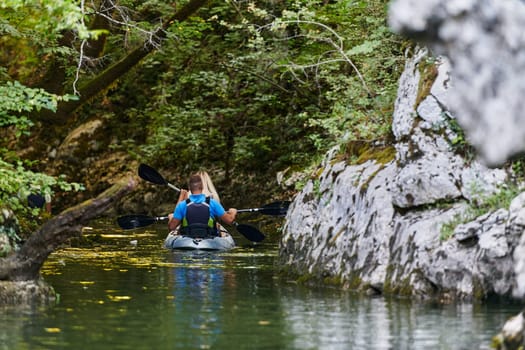 A young couple enjoying an idyllic kayak ride in the middle of a beautiful river surrounded by forest greenery.